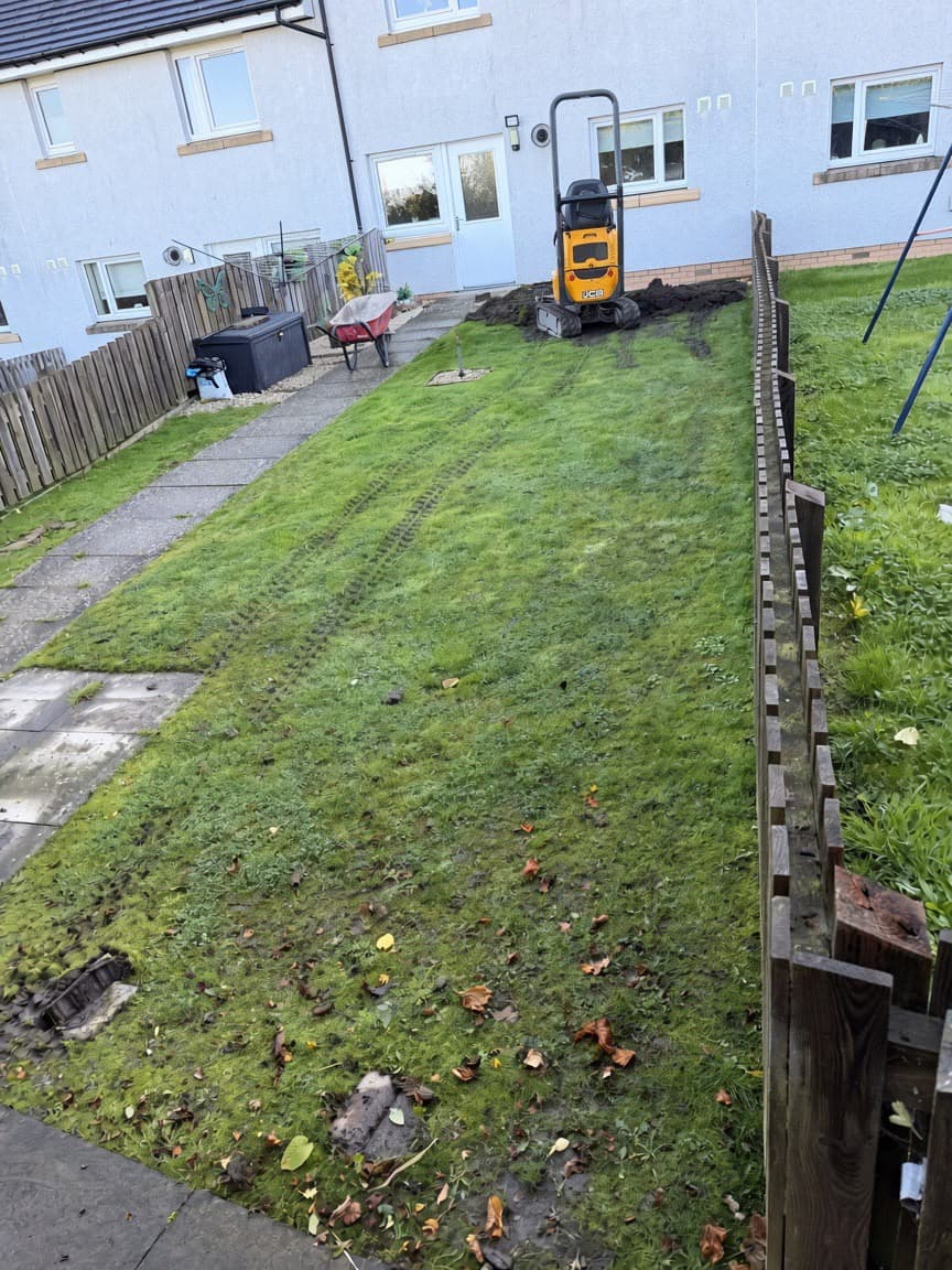 Mini digger arriving at the far end of the Chapelhall lawn, with rutted, moss-covered grass in front of it
