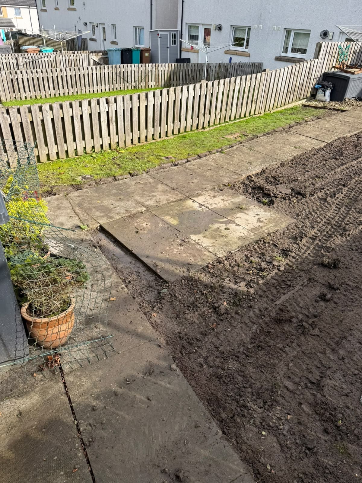 Water lying in the dug-out ground along the edge of the slab path, showing where the lawn had been holding water