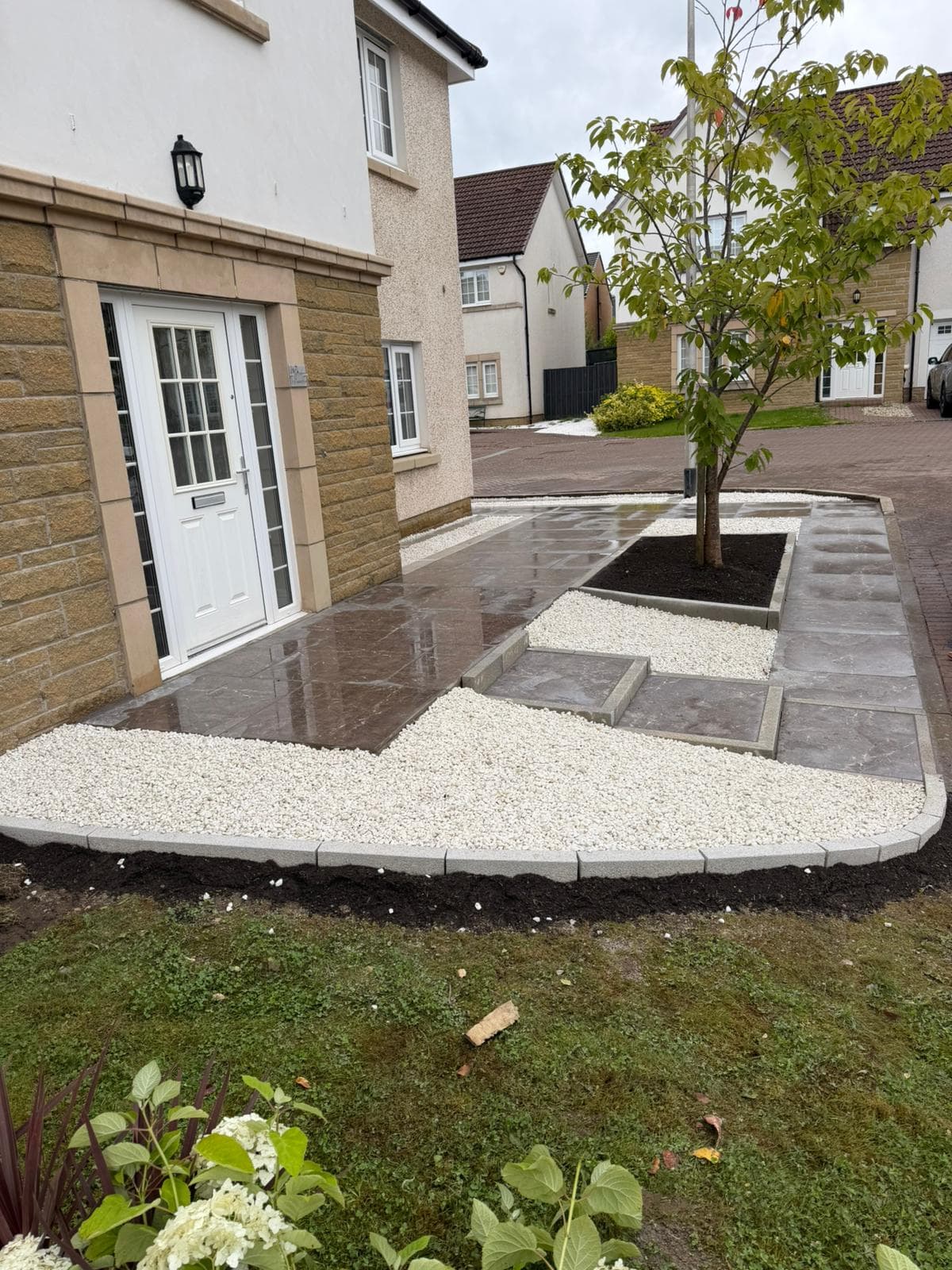 The same Dargavel frontage finished with dark porcelain paving, white decorative gravel and a curved granite kerb, with the cherry tree kept in a granite-edged bed