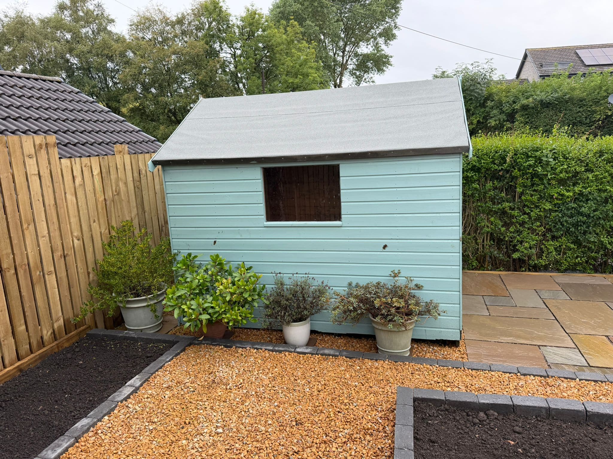 The same Glasgow rear garden finished with gold gravel, raised block-edged planting beds and a sandstone patio edge beside the repainted shed