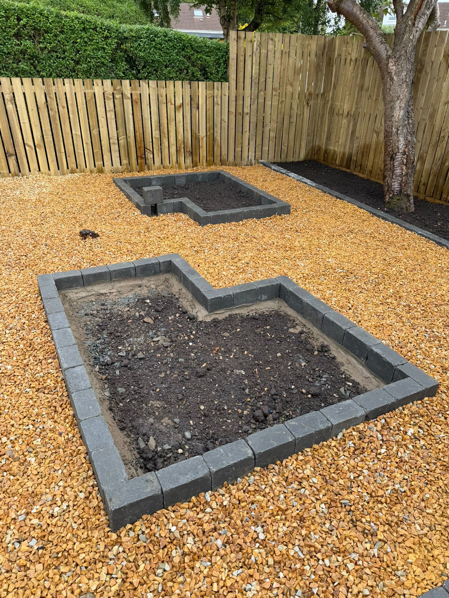 Two raised block-edged planting beds set in gold gravel in a rear garden