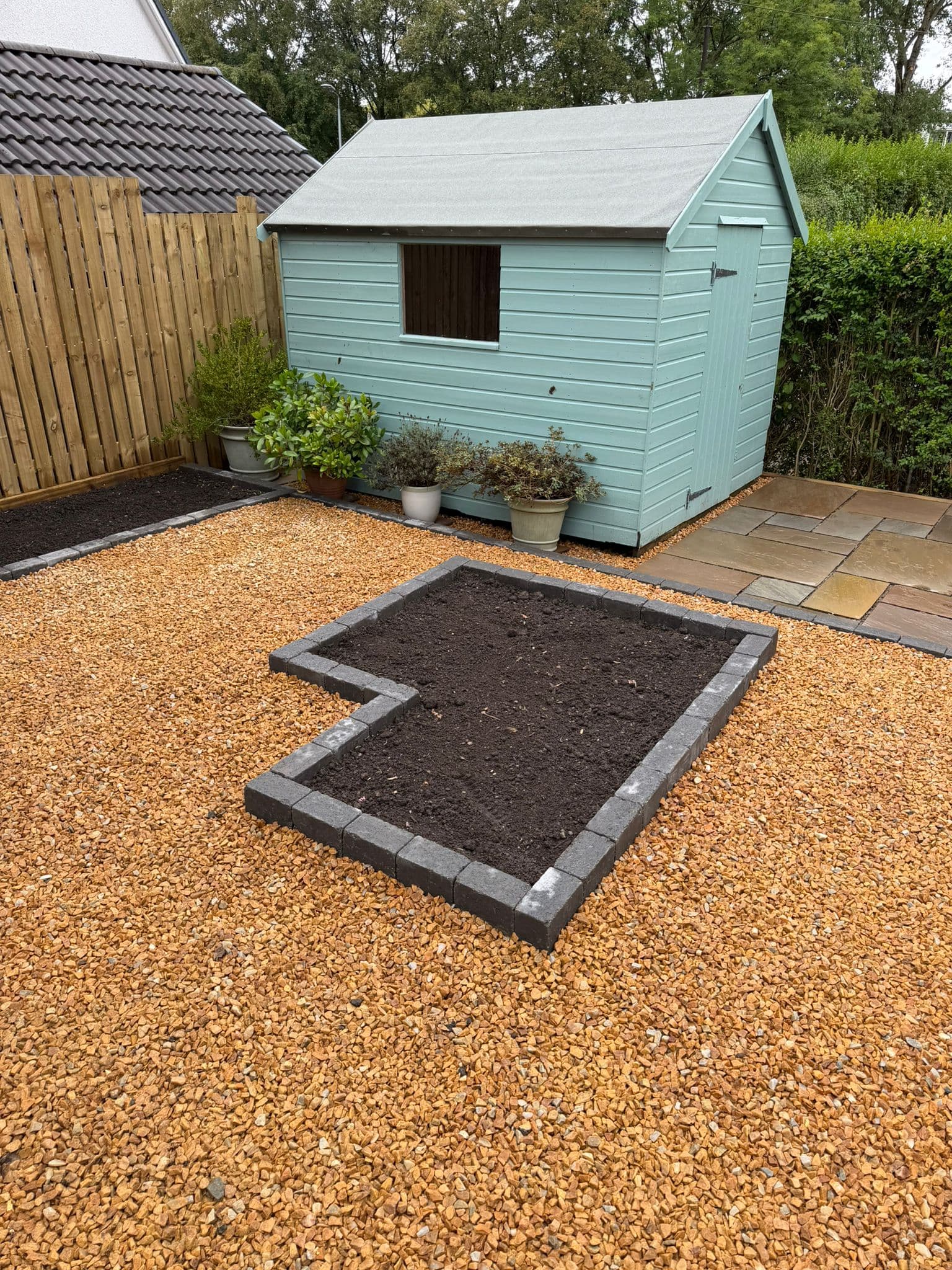 Wide view of a finished rear garden with sandstone patio, gravel and a painted garden shed